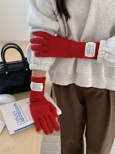 Red knitted touchscreen gloves worn by model, showing long ribbed cuff and brand tag