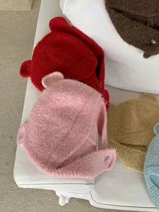 Detailed view of colorful knitted beanies with cute bear ears on a soft white sofa