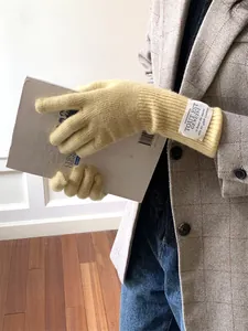 Detailed view of yellow knit gloves with a decorative fabric tag on the wrist.