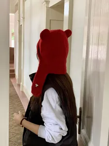 Red knitted beanie with cute bear ears and earflaps shown in a lifestyle indoor setting