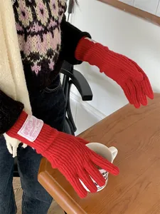Stylish red wool knitted gloves with a decorative patch shown in a cozy setting