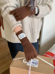 Close-up shot of elegant brown knit gloves worn by a model holding a cardboard gift box.
