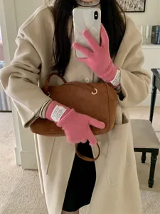 Lifestyle detail of warm pink knitted gloves with white label worn with a beige coat