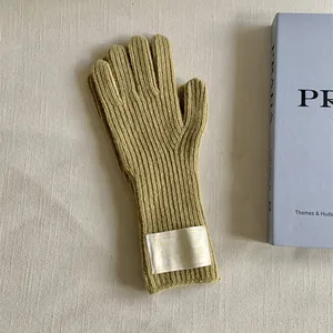 Close-up of mustard yellow knitted wool gloves with a decorative white cloth label.