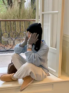 Woman wearing a cute black knitted bear ear hat with a cozy blue sweater and gray gloves