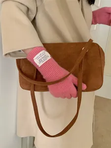 Close-up of a pink knitted winter glove with a white label held against a stylish brown bag