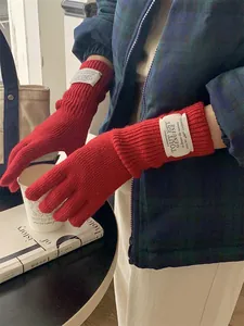 Close-up of red knitted long gloves with white logo patch worn in a lifestyle setting