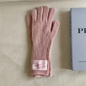 Close-up of pink knitted wool gloves with a vintage-style cloth label on the wrist.
