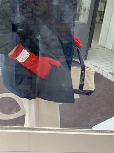 Detail shot of red knit winter gloves with white brand label paired with a plaid jacket.