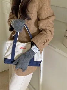 Close-up of grey imitation cashmere gloves worn by a model holding a canvas tote bag.