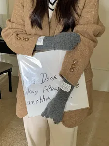 Detailed view of grey long knitted gloves with chic white tags on a model in camel coat