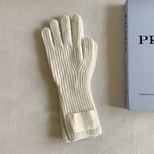 Detailed view of cream knitted wool gloves with a decorative fabric label on the wrist