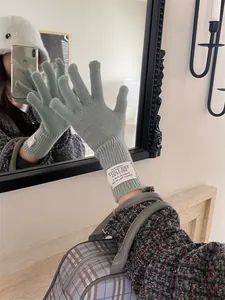 Detail of warm knitted sage green gloves with chic wrist label shown in a mirror selfie