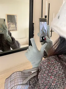 Close-up detail of sage green knitted touchscreen gloves worn for a stylish winter mirror selfie.