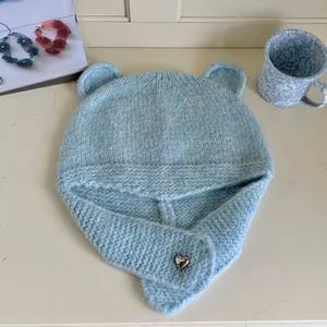 Macro detail of a light blue knitted winter hat featuring cute bear ears and a silver heart pin