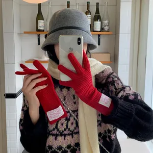 Elegant warm red knitted wool gloves with stylish fabric labels for trendy winter fashion outfits.