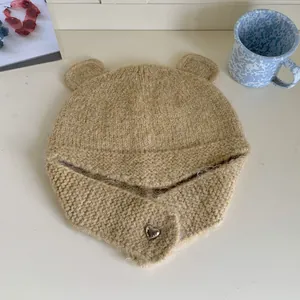 Detailed macro view of beige knitted bear ear hat featuring heart-shaped button decor