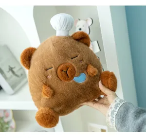 Niedliche braune Wasserschwein-Plüschpuppe mit weißer Kochmütze in der Hand