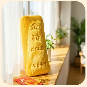 Détail d'un coussin en peluche lingot d'or avec texte brodé sur un rebord.