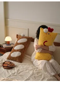 Gros plan de coussins en peluche longs jaune crevette et marron baguette sur un lit