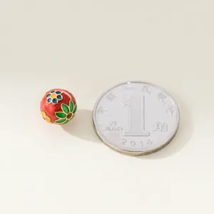 Macrodetail van een 8mm rode emaille bloemkraal met een munt voor schaalreferentie