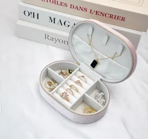 Internal detail of a soft pink oval velvet jewelry box showing organized rings and necklace