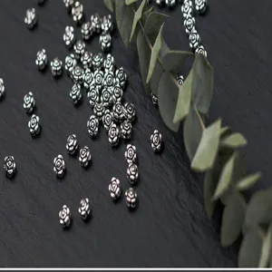 Close-up of S925 silver rose-shaped spacer beads on a slate background with eucalyptus