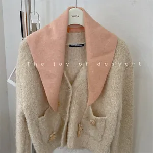 Close-up view of a soft pink wool blend triangular knit scarf styled on a beige cardigan