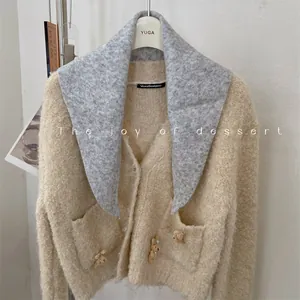 Detail view of a stylish wool knit triangle scarf paired with a beige teddy bear cardigan.