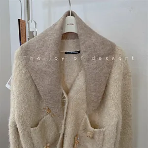 Detailed view of a soft beige knit cardigan paired with a brown triangle scarf collar.