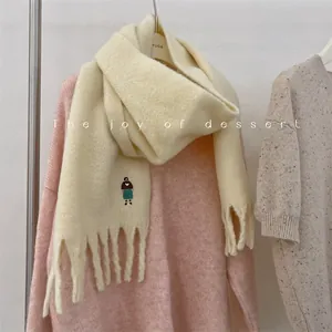 Detailed view of cream wool blend scarf featuring cute girl embroidery and fringe detail.