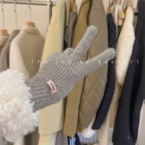 Close-up of grey knitted winter glove featuring a white fluffy cuff and pink brand tag