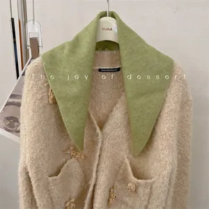 Detail of a beige knit cardigan with cute small bear accents and a green triangular scarf.
