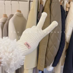Close-up of white knitted gloves with fluffy lamb wool cuffs and a small pink tag.