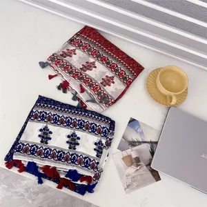 Detailed view of two folded ethnic-style scarves with tassels on a white marble table.