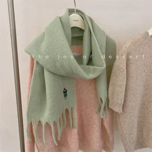 Detail of soft green wool blend scarf with embroidered girl motif and tassels