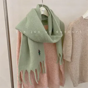 Close-up detail of cute girl embroidery on a soft sage green wool blend fringed winter scarf