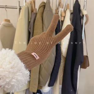 Close-up detail of brown knitted glove featuring plush white faux fur cuff and pink brand label