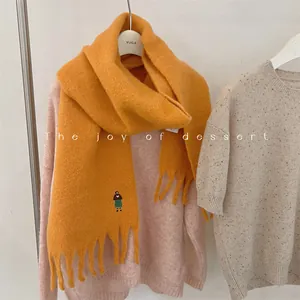 Close-up of orange wool blend scarf with fringe and cute embroidered girl design.
