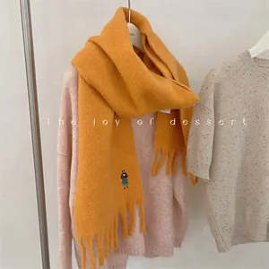 Close-up of orange wool blend fringe scarf with cute girl embroidery detail for winter