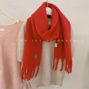 Close-up of a red wool-blend scarf featuring a cute embroidered girl motif and fringe