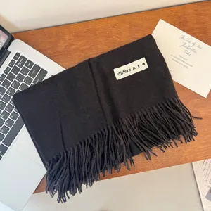 Detailed view of a black winter scarf with fringe and a white label on a wooden desk