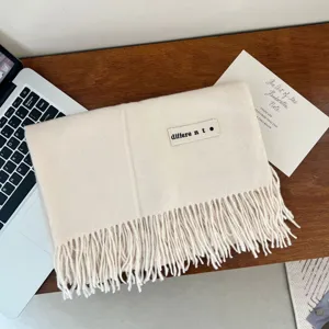 Detail of a cream imitation cashmere scarf with fringe and a minimalist label on a wooden desk