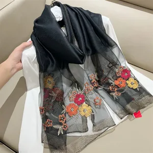 Detailed view of black silk blend scarf with colorful floral embroidery and metallic edges.