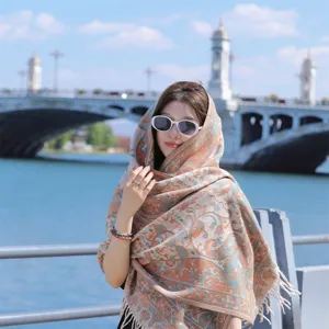 Model wearing a thick ethnic paisley shawl with tassels against a river bridge background