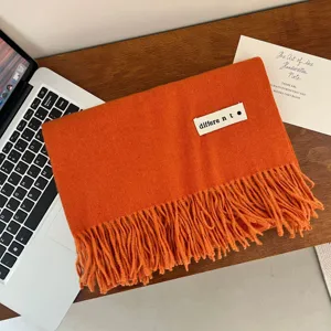 Detailed view of a soft orange imitation cashmere fringe scarf on a wooden desk