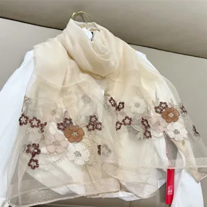 Macro view of exquisite begonia flower embroidery on a soft silk blend beige scarf.