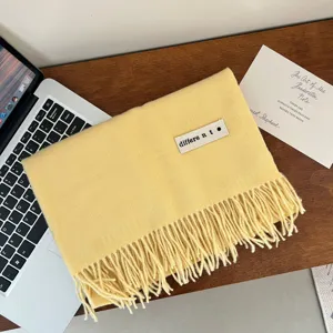 Soft yellow fringed imitation cashmere scarf displayed on a wooden desk next to a laptop.