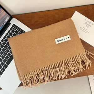 Close-up detail of a soft camel-colored winter scarf featuring a white brand label