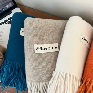 Collection of soft solid color thick faux cashmere scarves with fringe on a wooden table